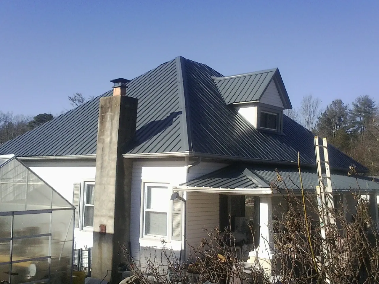 Dark blue standing seam metal roof on a white farmhouse with dormer — Slate & Tile Roof Repair by Roofing Brothers in Interlochen