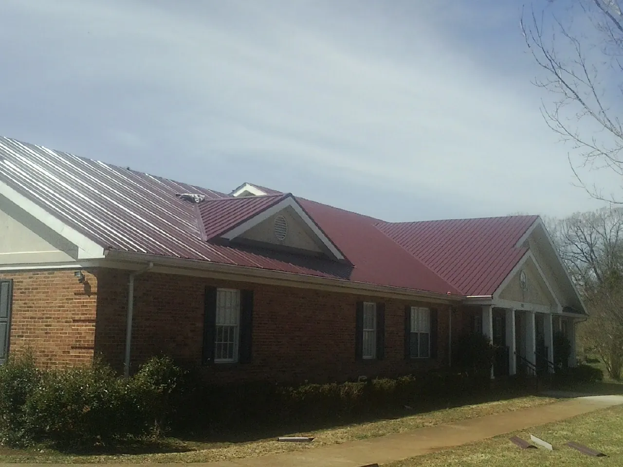 Red metal roof with gabled entries on a long brick building, from a Hail Damage Roof Repair job in Interlochen