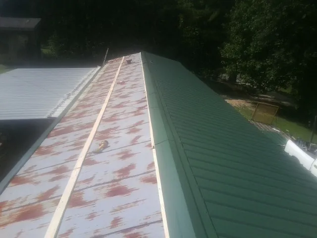 Old rusted panels beside newly installed green metal roofing — Wind Damage Roof Repair by Roofing Brothers in Interlochen