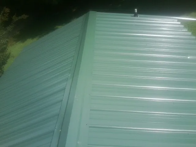 New green metal panels meeting at the ridge of a roof — Flat Roof Repair work by our crew in Interlochen