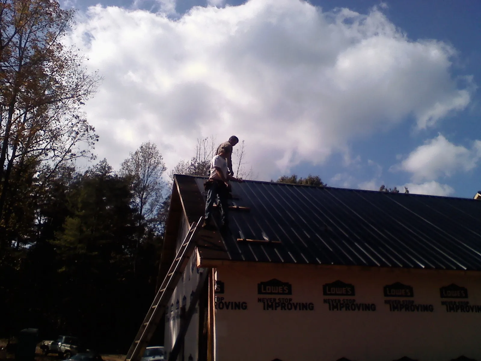 Roofer fastening dark metal panels high against a cloudy sky, from a Roof Inspection job in Interlochen